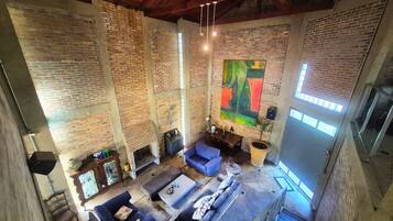 Um loft espaçoso com paredes de tijolo aparente, uma grande pintura abstrata e um mezanino com área de estar.