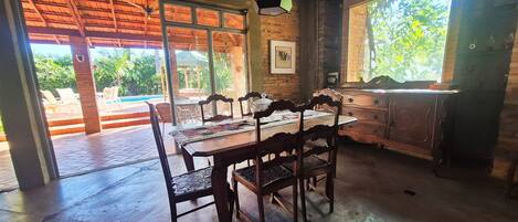 A dining area with a wooden table and chairs, a view of a pool outside, and a brick wall.