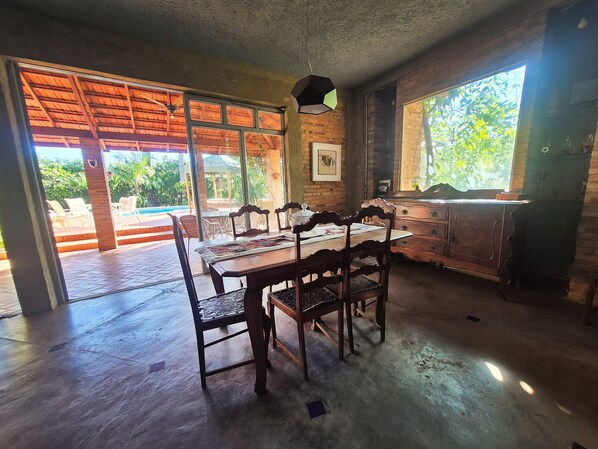 A dining area with a wooden table and chairs, a view of a pool outside, and a brick wall.