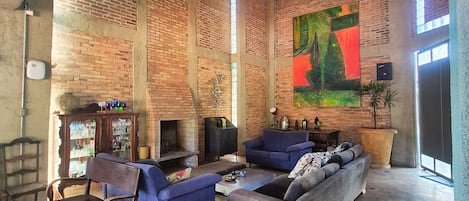 A spacious living area with brick walls, a fireplace, and a large painting.