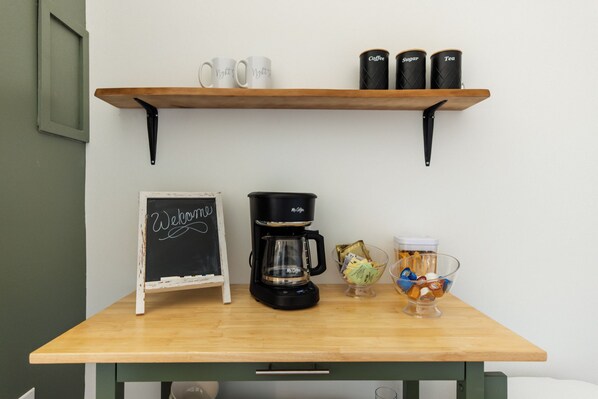 A coffee station with a coffee maker, mugs, and containers labeled coffee, sugar, and tea.