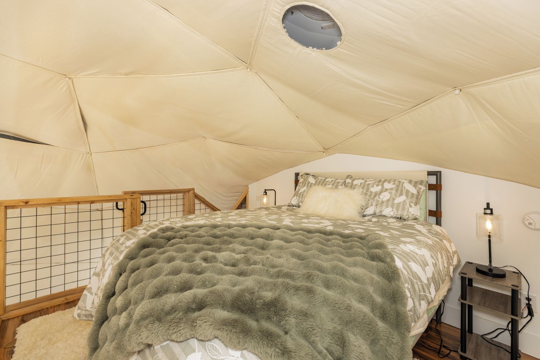 A cozy tented room with a bed, a small table, and a lamp.