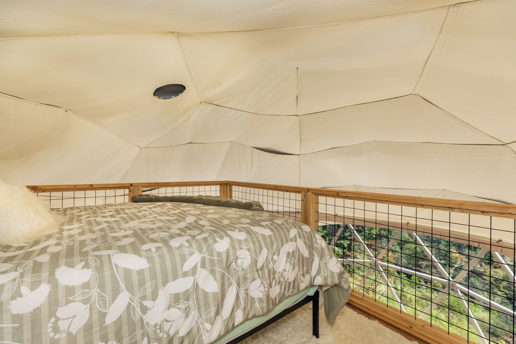 A tent with a bed, a window, and a view of greenery outside.
