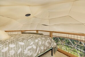 Ein Zelt mit Bett, Fenster und Blick auf grüne Natur.