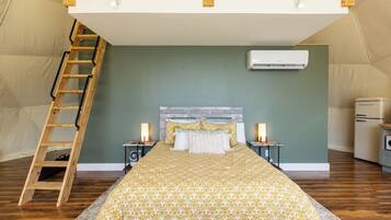 A tented room with a bed, a ladder, a fan, and a refrigerator.