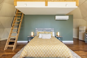 Una habitación con tienda de campaña, una cama, una escalera, un ventilador y un refrigerador.