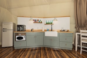 Cocina compacta equipada con refrigerador, microondas, horno y pileta. Posee dos luces colgantes, una cubierta de madera y un ventanal con cortinas.