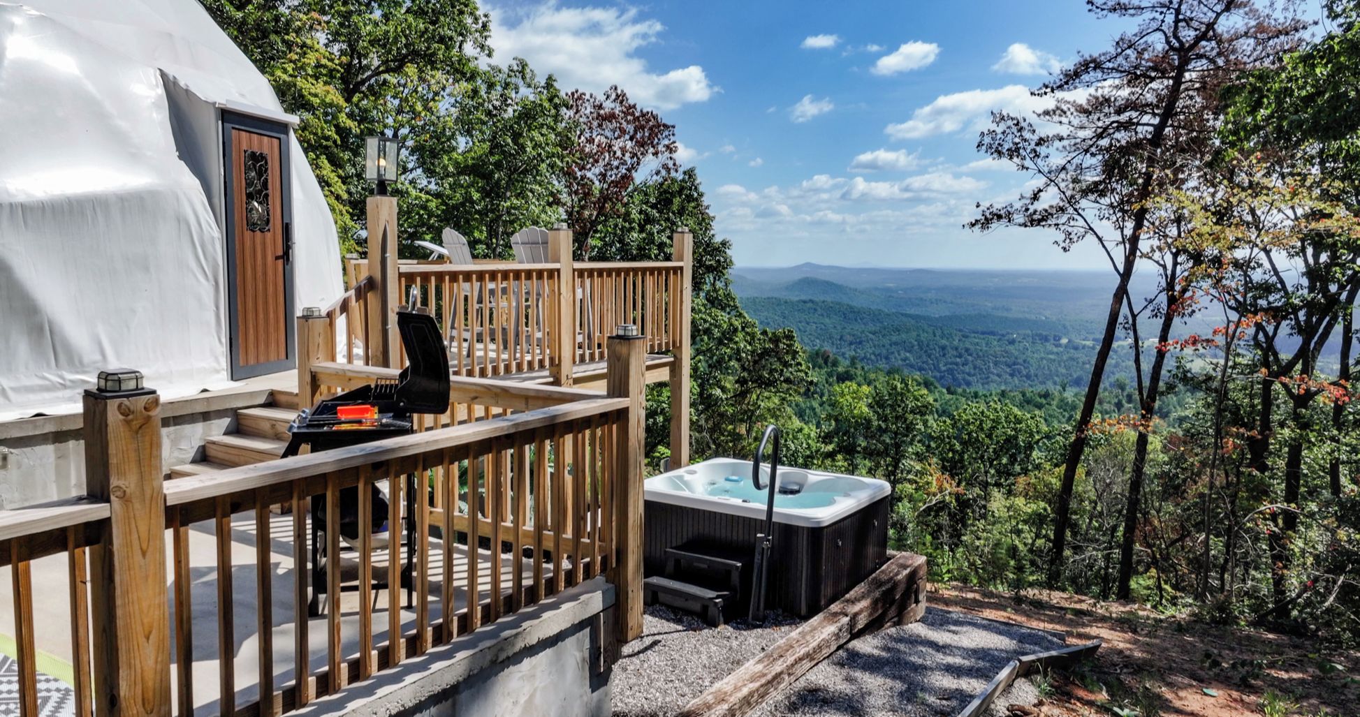 Eine Holzterrasse mit Whirlpool und Sitzgelegenheit, mit Blick auf ein bewaldetes Tal.