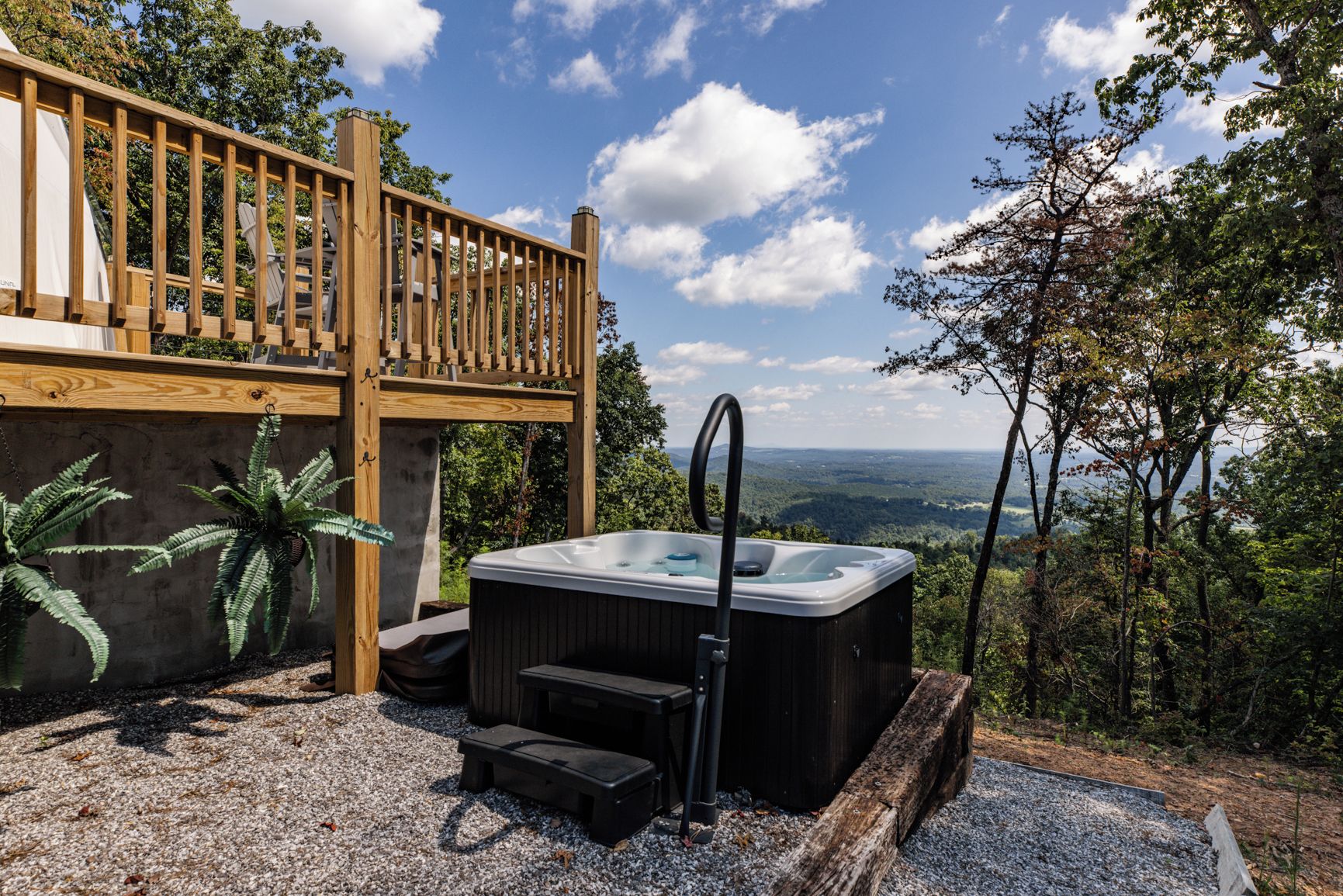 A hot tub with steps, a wooden deck, and a view of the landscape.