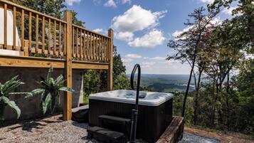 A hot tub with steps, a wooden deck, and a view of the landscape.
