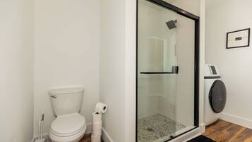 A bathroom with a toilet, a glass-enclosed shower, and a washing machine.