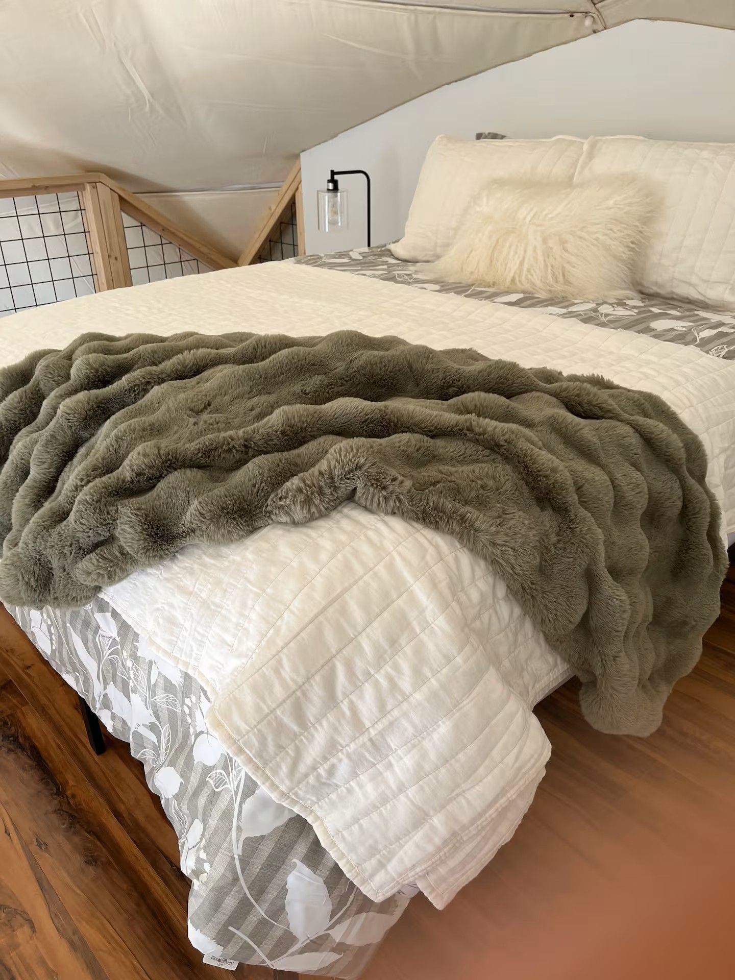 Een slaapkamer met een bed, een wit geborduurde beddeken, een zachte groene deken en een wit kussen.