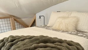 A bedroom with a bed, a white quilted bedspread, a fluffy green blanket, and a white pillow. - Charming 2-bedroom cabin with AC in peaceful Hays (Hays)