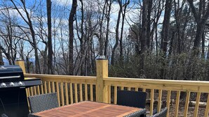 Une terrasse extérieure avec une table en bois et des chaises en osier, entourée d’un tapis à motifs et d’une rambarde en bois.