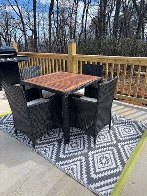 An outdoor patio with a wooden table and wicker chairs, surrounded by a patterned rug and a wooden deck railing. - Charming 2-bedroom cabin with AC in peaceful Hays (Hays)