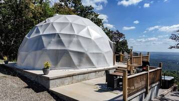 A geodesic dome structure with a patio area, outdoor seating, and a scenic view.