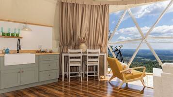 A room with a dining area, a telescope, and a view of the landscape.