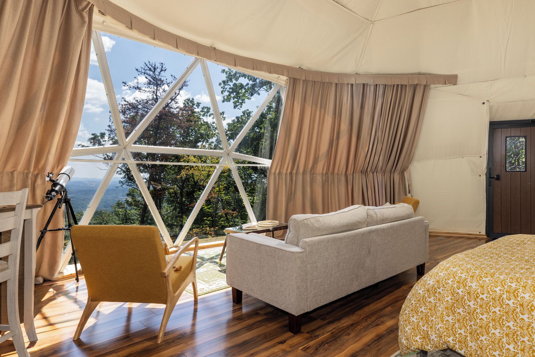 A bedroom with a large window, a telescope, a sofa, and a bed.
