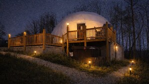 Une structure en forme de dôme, dotée d’une terrasse et d’une rambarde en bois, entourée d’un chemin de gravier et d’arbres.