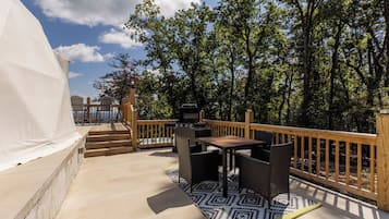 An outdoor deck with a grill, wicker furniture, and a view of the forest.