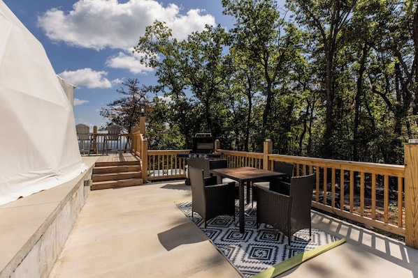 Una terraza exterior con una parrilla, muebles de mimbre y vistas al bosque.