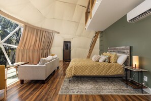 A bedroom with a bed, a sofa, a bedside table, and a window with curtains.