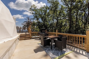 Eine Terrasse im Freien mit Grill, Korbmöbeln und Blick auf den Wald.