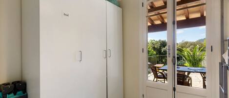 A room with a white wardrobe, a door leading to an outdoor area with a table and chairs, and a small trash bin.