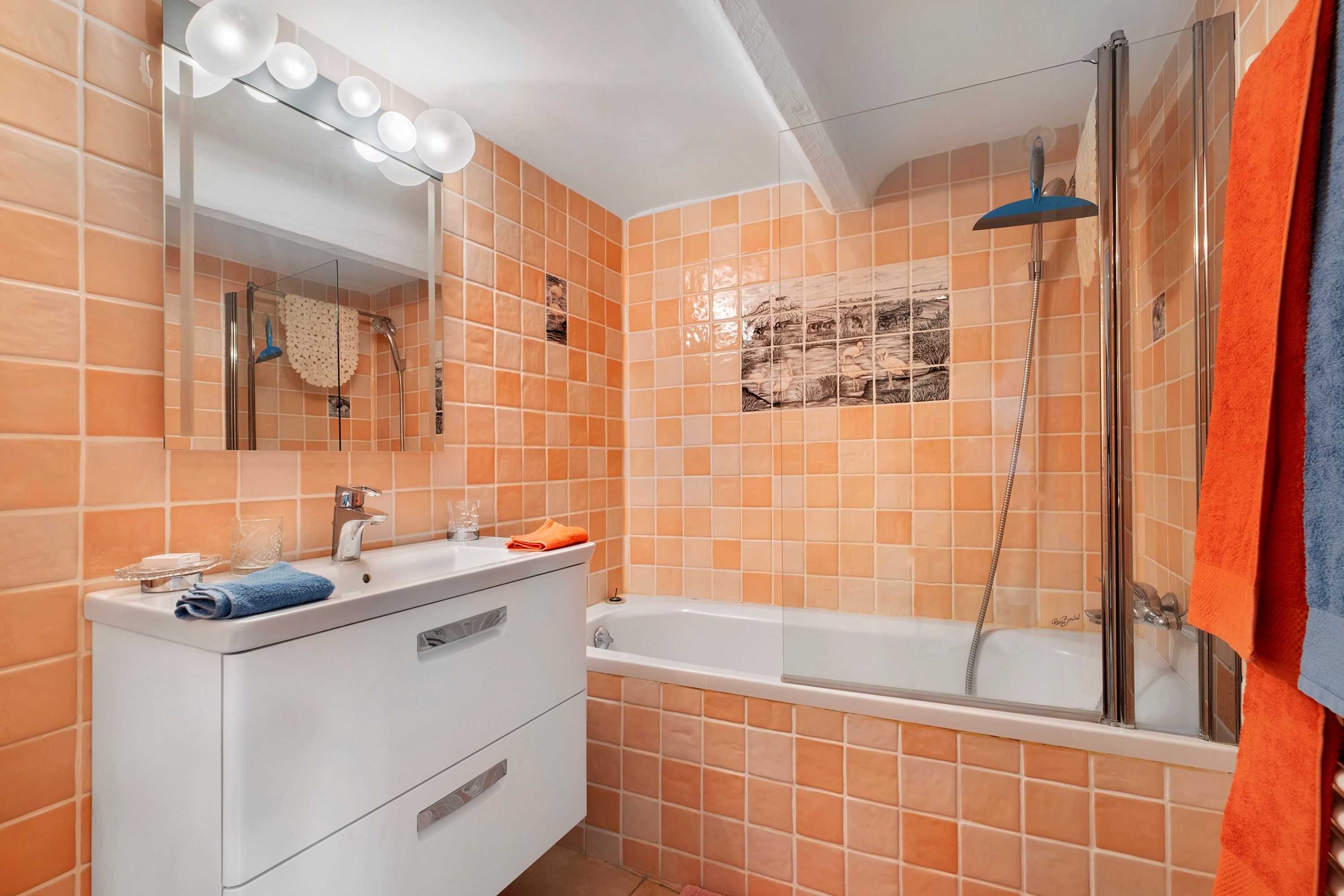 A bathroom with orange tiles, a white vanity with a mirror, a bathtub, and a shower.
