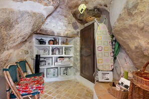 A rustic stone-walled room with a wooden door, shelves with kitchenware, a wicker chair, and a patterned shower curtain. - Holiday Home 'Au Bon Accueil' with Mountain View, Private Terrace and Wi-Fi (Fayence)