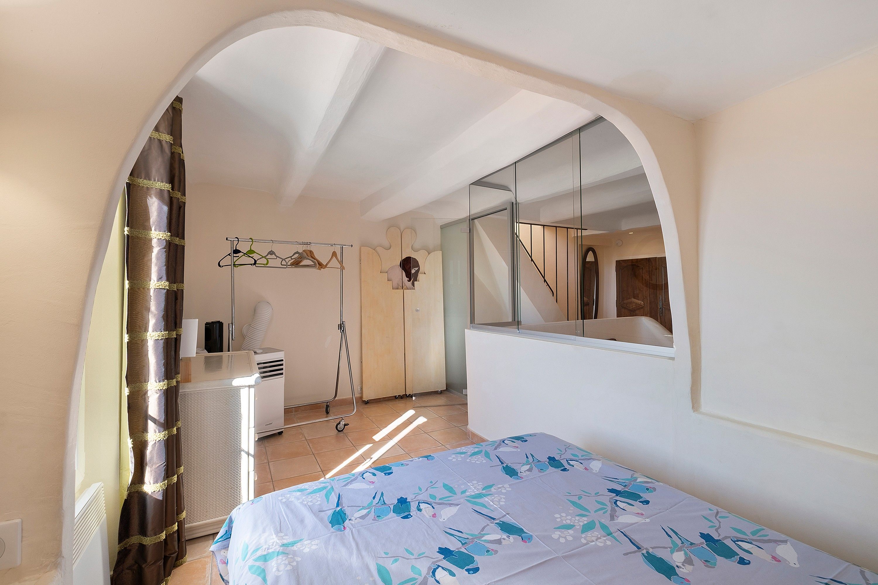 A bedroom with a bed, a mirror, a radiator, and a window with curtains.