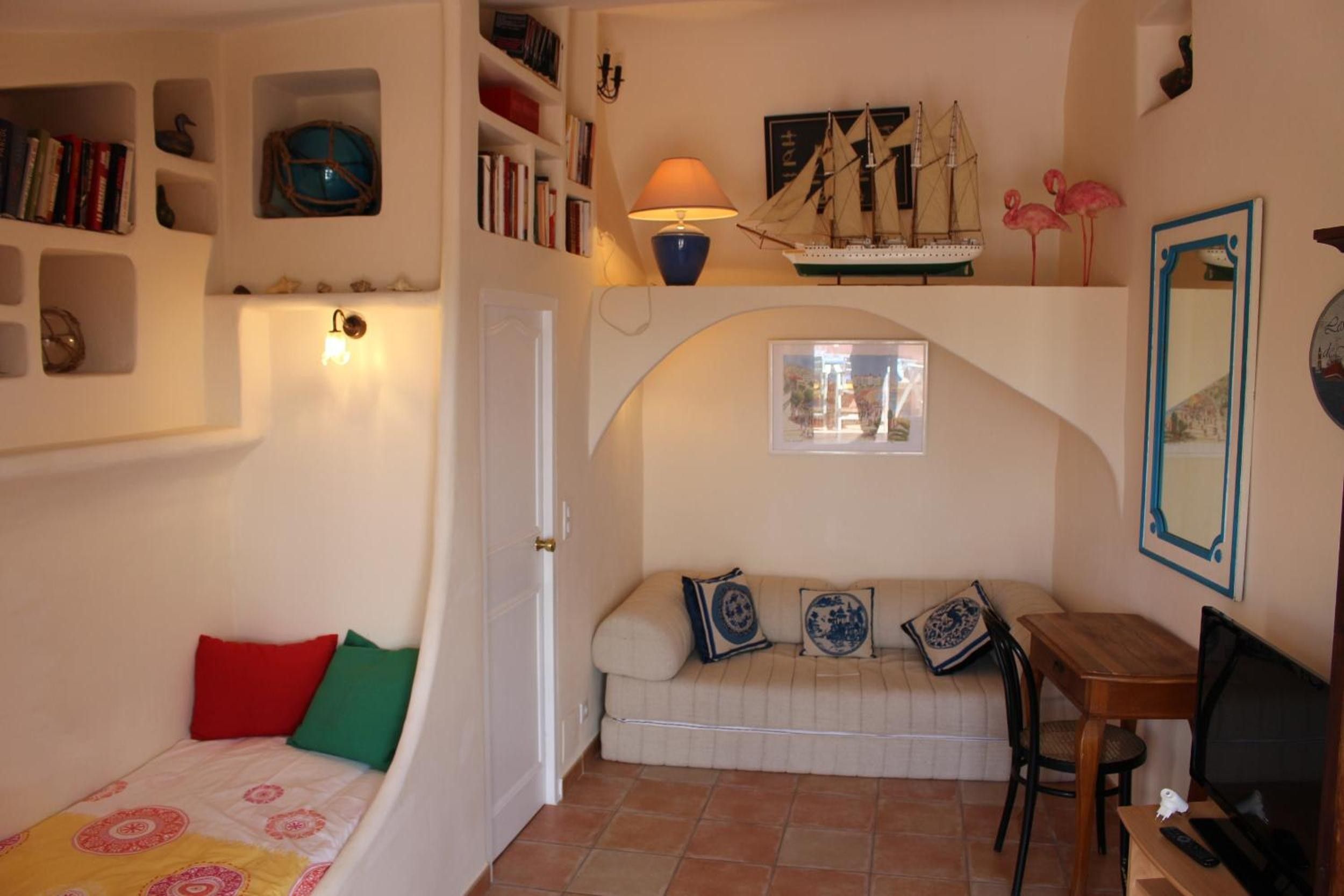 Une pièce confortable avec un canapé, une petite table, une lampe, une bibliothèque et une maquette de bateau.