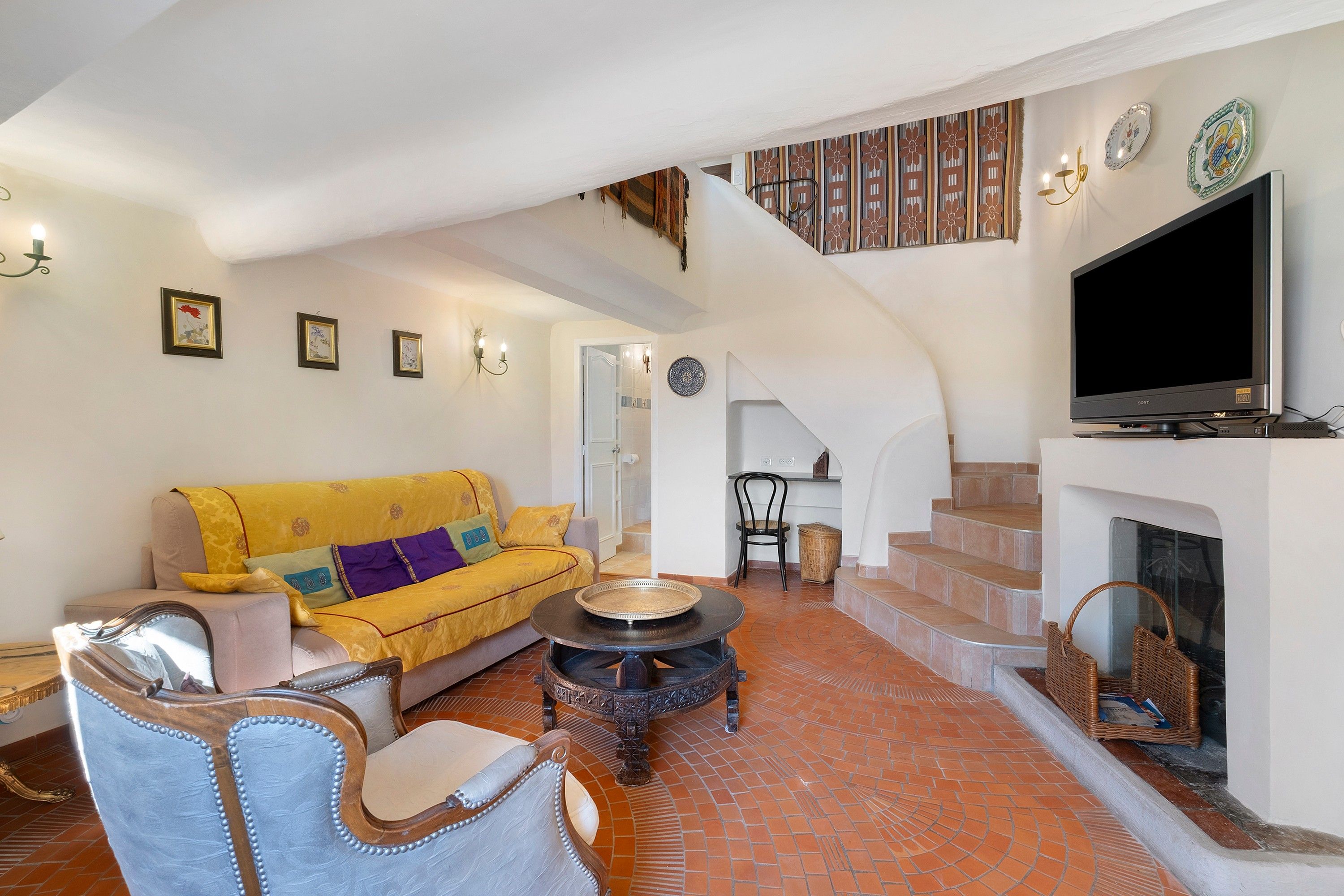 A spacious living area with a yellow sofa, a fireplace, a television, and a staircase leading to an upper floor.