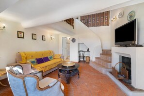 A spacious living area with a yellow sofa, a fireplace, a television, and a staircase leading to an upper floor. - Holiday Home 'Au Bon Accueil' with Mountain View, Private Terrace and Wi-Fi (Fayence)