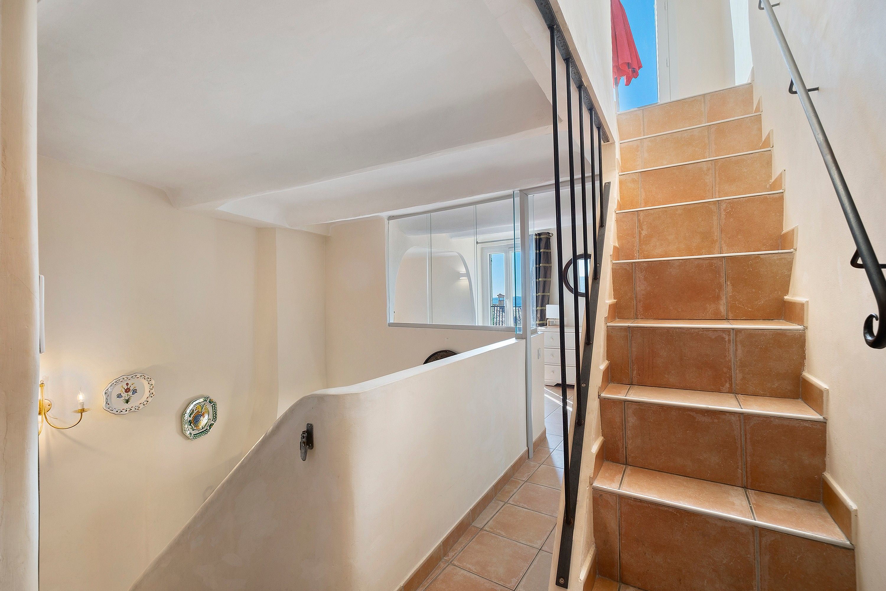 Un escalier avec une rampe, un palier avec une porte vitrée, et un mur avec un interrupteur et des plaques décoratives.