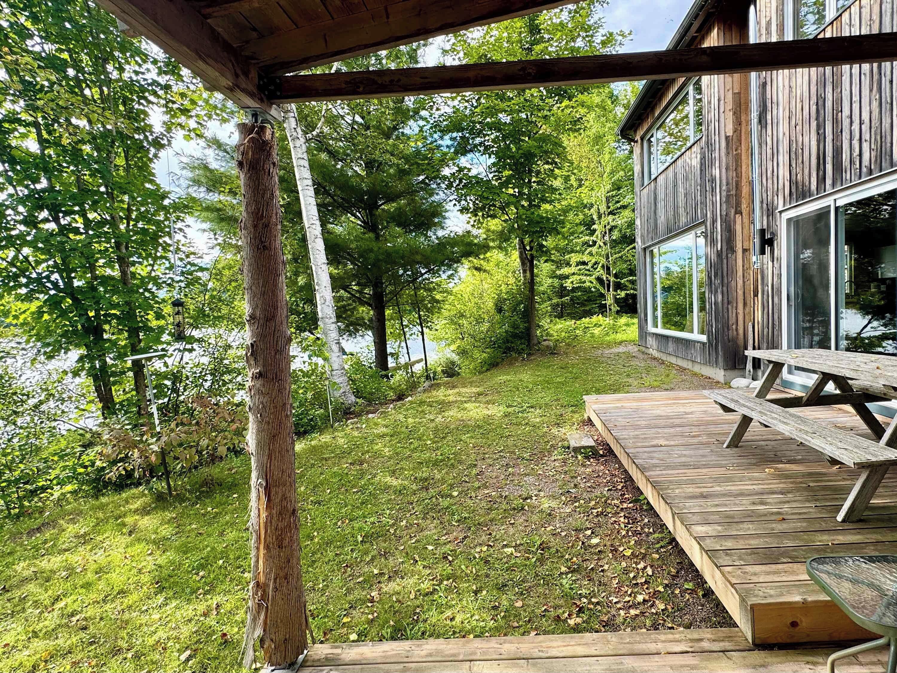 A wooden deck with a picnic table, surrounded by a grassy area and trees.