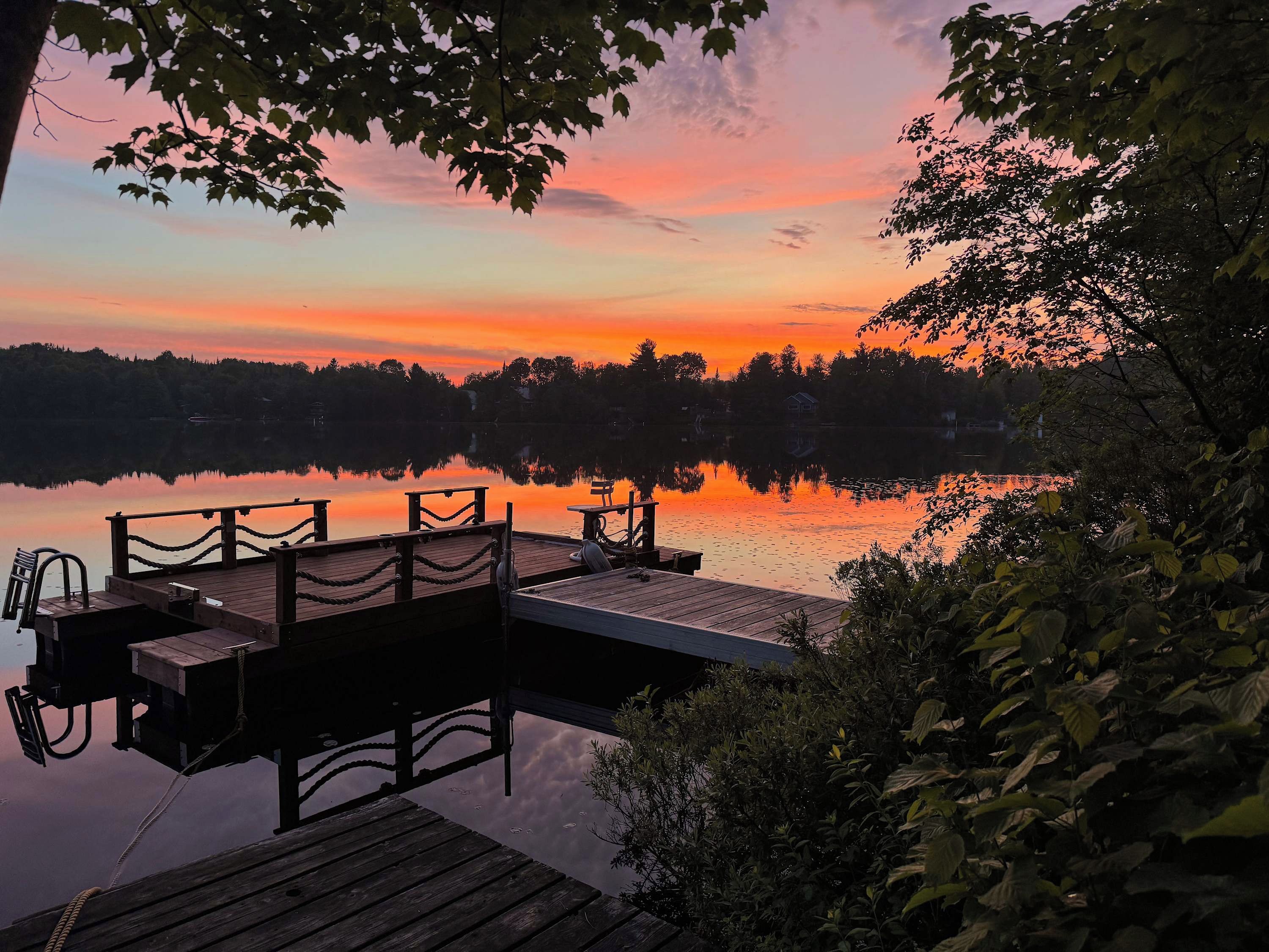 A wooden dock extending into a calm lake with a sunset in the background.