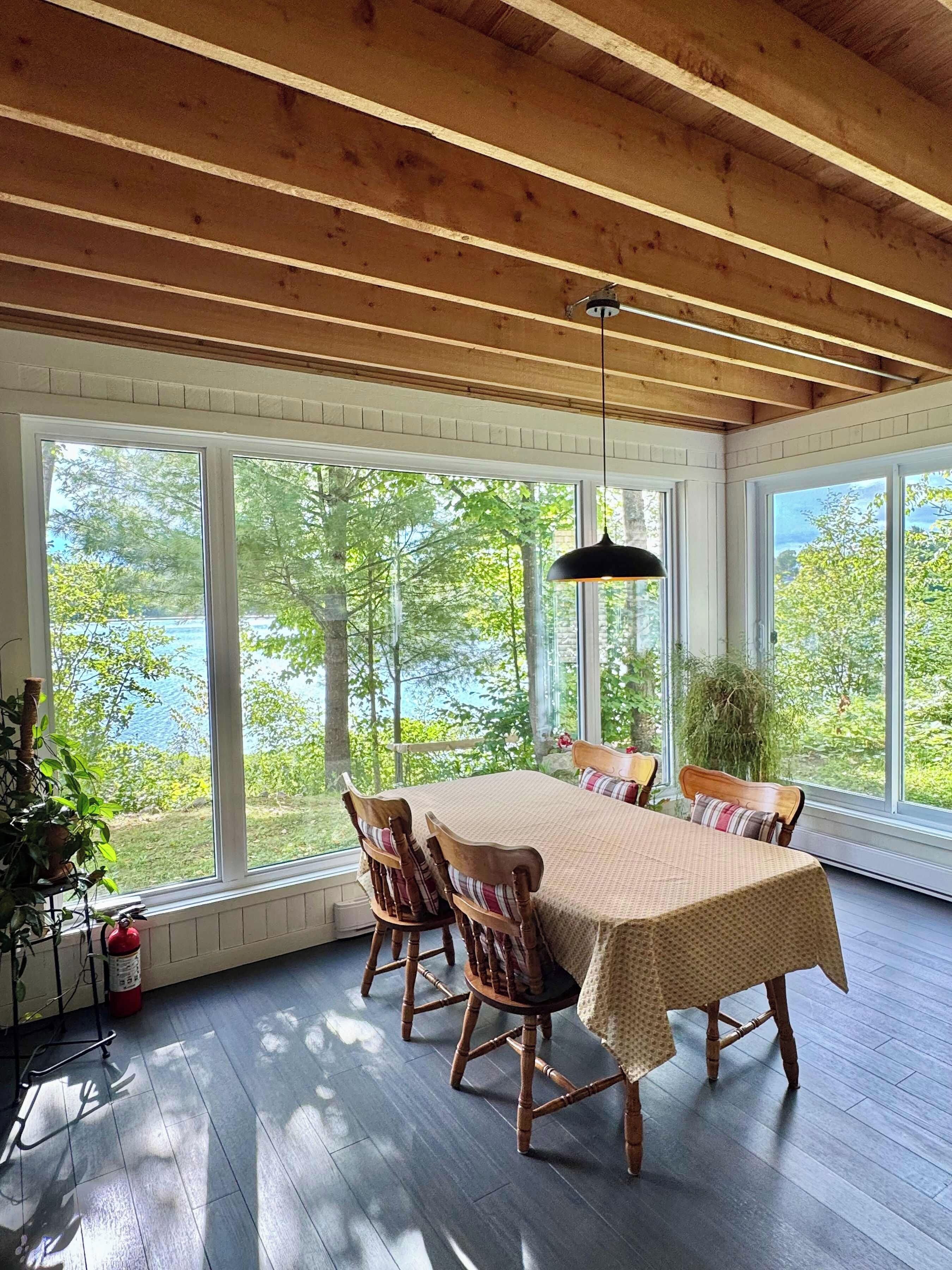 A dining area with a table and chairs, large windows, and a view of trees and water.
