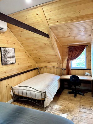 A small, cozy room with a sloped ceiling, a single bed, a desk with a chair, and a window with curtains.