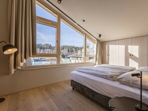 A bedroom with a large window, a bed, a bedside table, and a lamp. - Premium Penthouse With 3 Bedrooms (Oberndorf in Tirol)