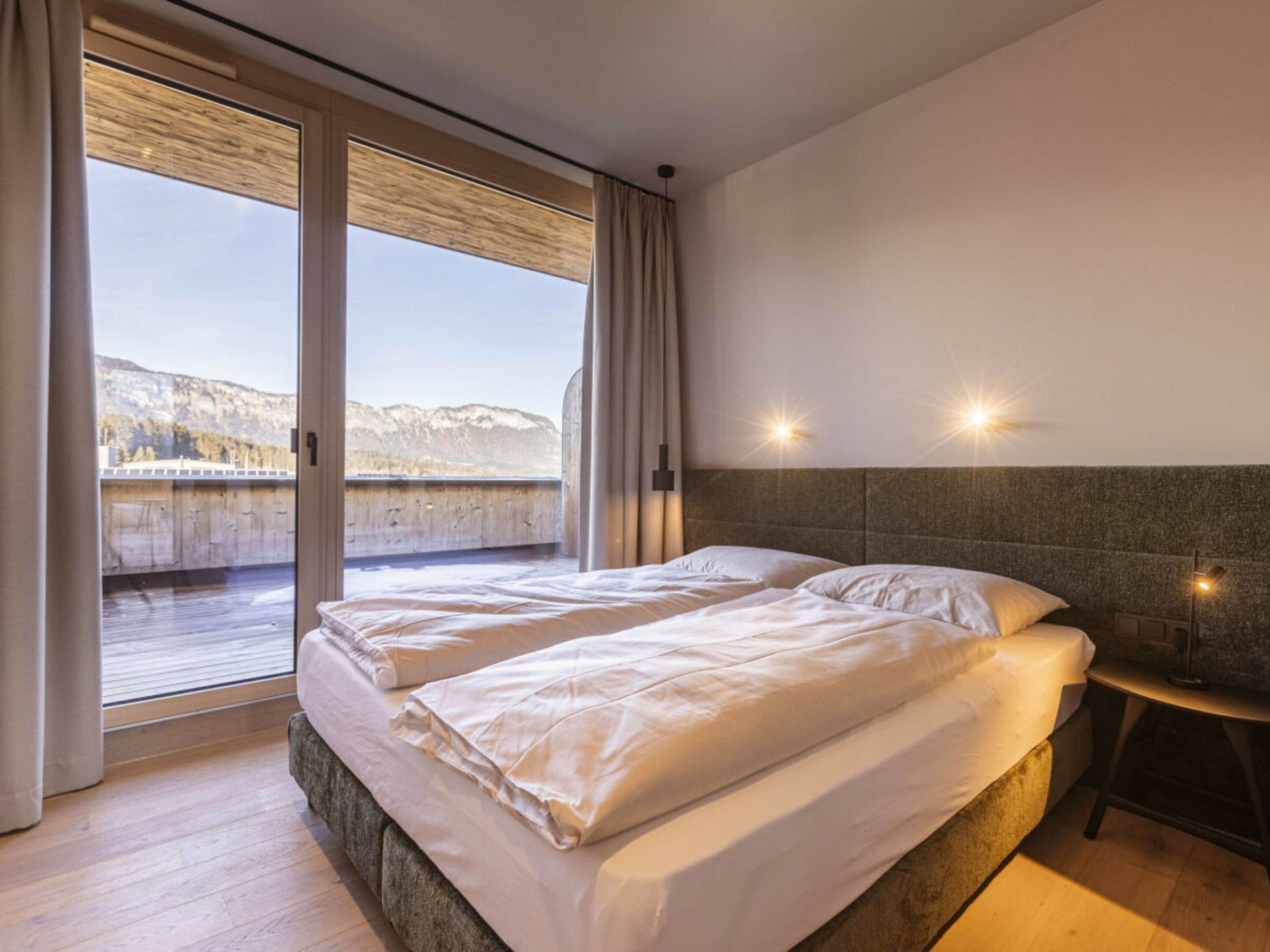 A bedroom with two beds, a view of mountains, and a sliding glass door.
