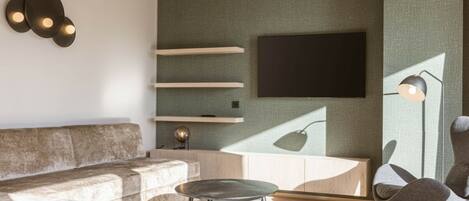 A modern living room with a sectional sofa, a round coffee table, and a flat-screen TV mounted on a textured wall.