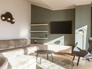 A modern living room with a sectional sofa, a round coffee table, and a flat-screen TV mounted on a textured wall. - Premium Penthouse With 3 Bedrooms (Oberndorf in Tirol)
