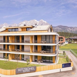 Un hotel de varios pisos con un letrero que dice 'Kitzbühel Suites' y un paisaje montañoso de fondo.
