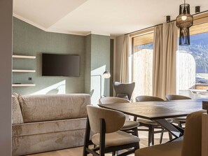 A modern dining area with a wooden table and chairs, a flat-screen TV mounted on the wall, and a view of a mountainous landscape through large windows. - Premium Penthouse With 3 Bedrooms (Oberndorf in Tirol)