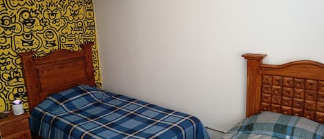 A bedroom with a wooden bed, a nightstand with a lamp, and a wall with a yellow patterned design.