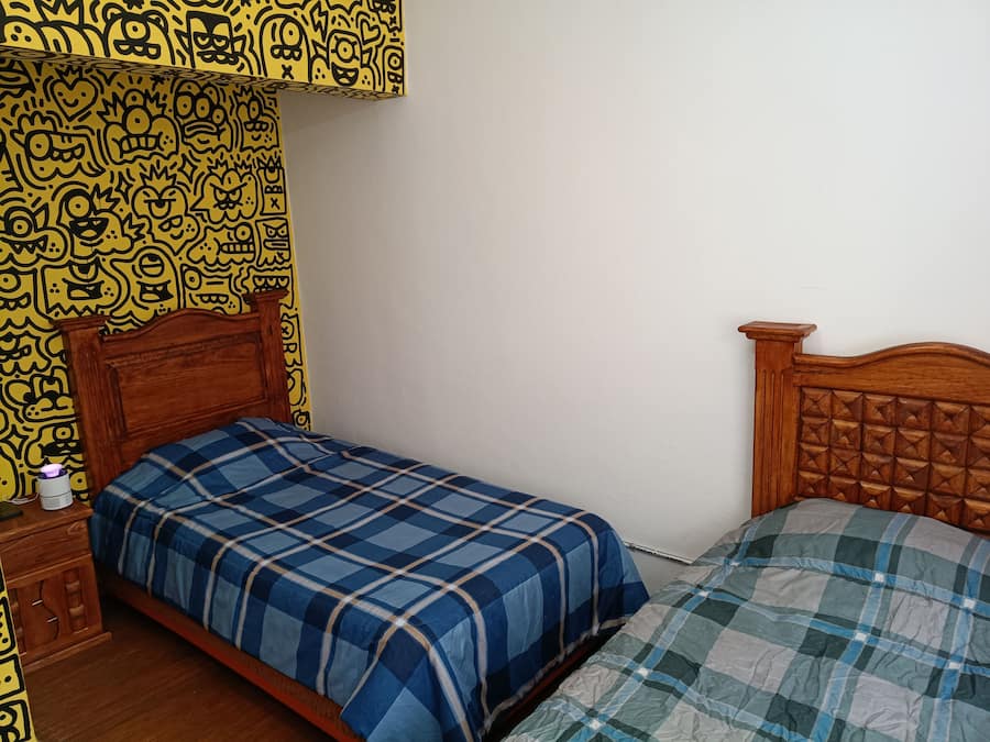 Un dormitorio con una cama de madera, una mesita de noche con lámpara y una pared con diseño amarillo y estampado.
