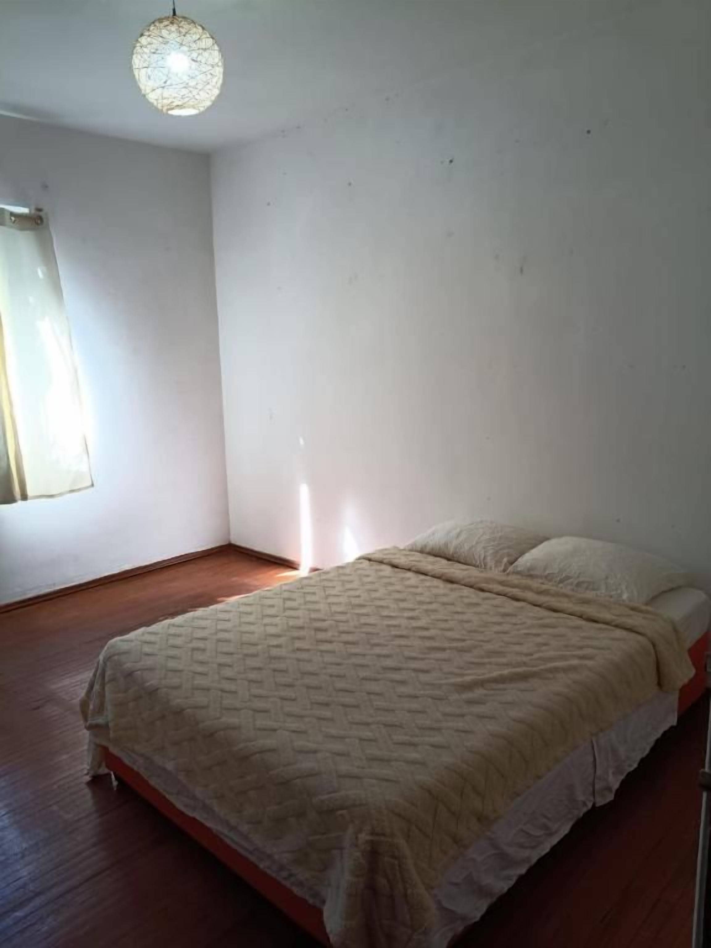 A room with a bed, a window, and a hanging light fixture.