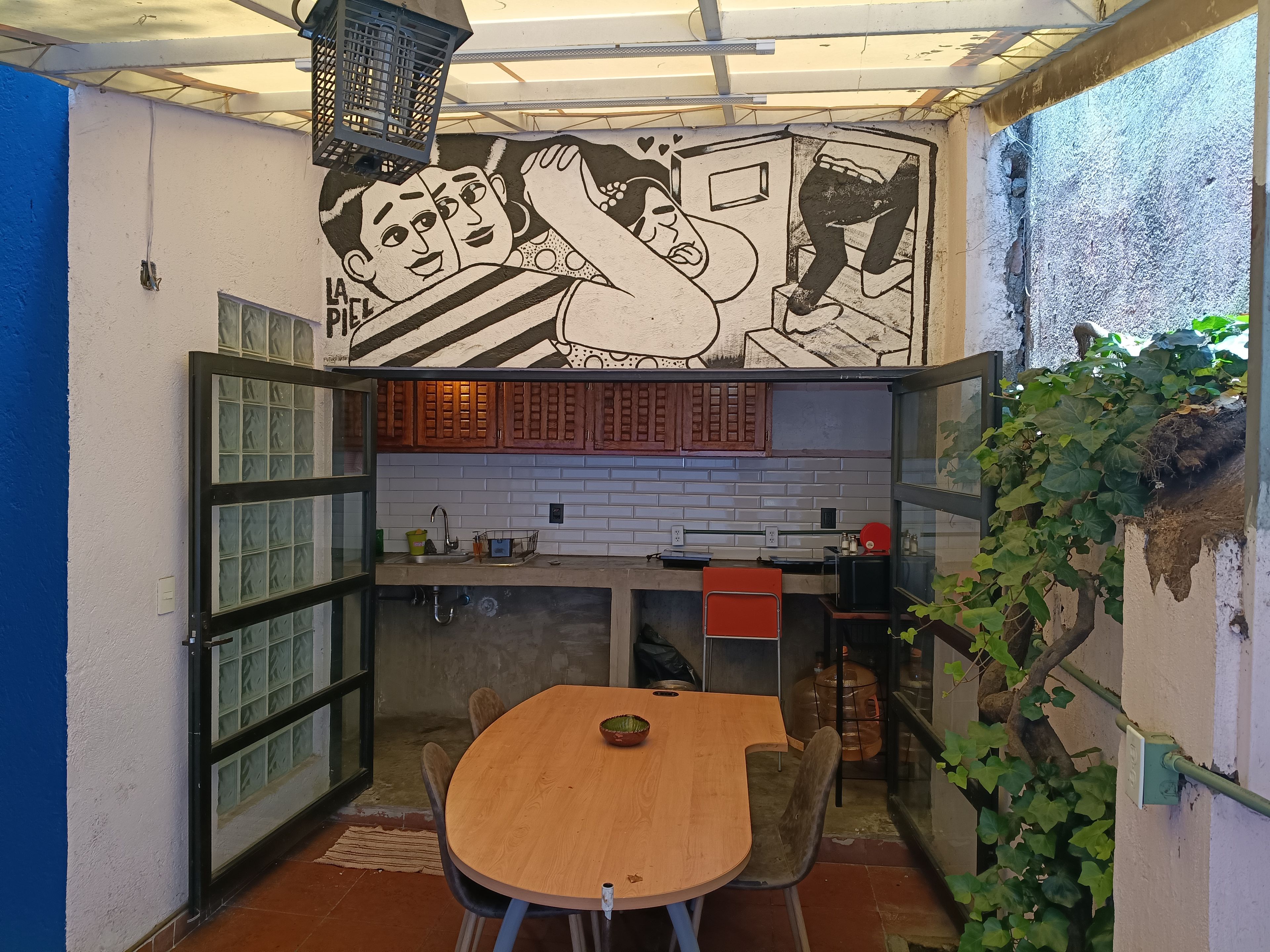 A compact kitchen with a dining area, featuring a mural, wooden cabinets, and a tiled backsplash.