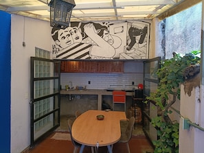 Une cuisine compacte avec un coin repas, agrémentée d’une fresque murale, de meubles en bois et d’un pare-feu en carreaux.